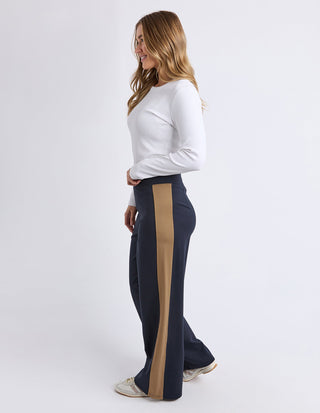 Woman wearing white long sleeve top and navy blue wide leg pants with tan side stripe.