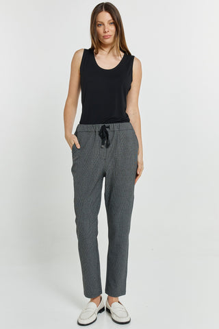 Woman wearing a black sleeveless top, grey textured trousers, and white loafers.