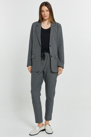 Woman wearing a grey textured blazer and matching trousers set with white loafers.