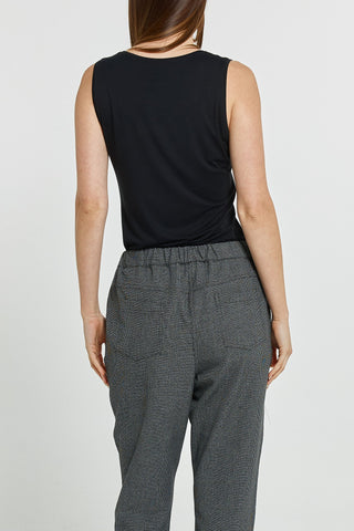 Rear view of a woman wearing a black sleeveless top and grey patterned trousers.
