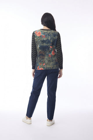 Woman wearing a floral print long sleeve top with dark blue trousers and white sneakers.