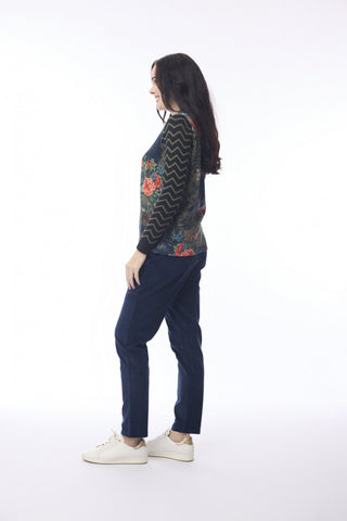 Woman wearing a floral patterned long sleeve top and navy blue trousers with white sneakers.