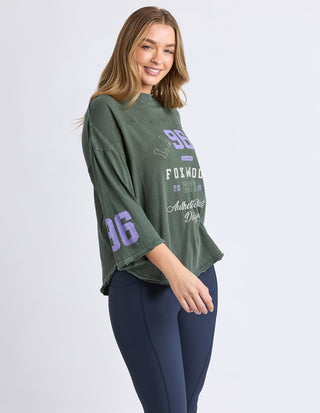 Woman wearing an oversized olive green Foxwood graphic sweatshirt and navy leggings.