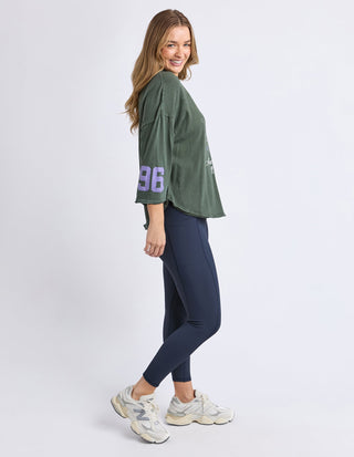 Woman wearing an olive green oversized graphic sweatshirt, navy blue leggings, and white sneakers.
