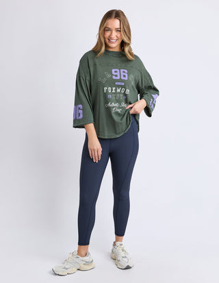 Woman wearing an oversized olive green Foxwood sweatshirt and navy blue leggings.