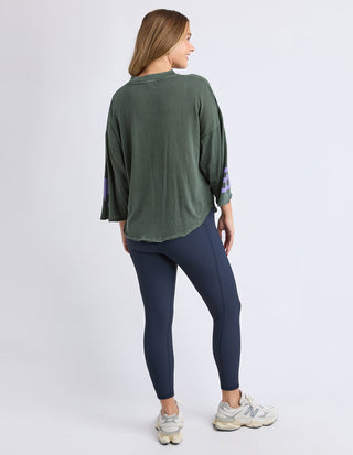 Woman wearing an oversized olive green sweatshirt and navy blue leggings with white sneakers.