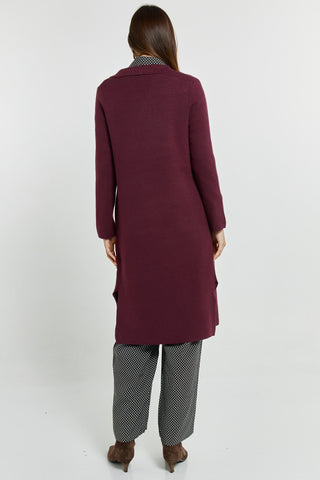 Rear view of a woman wearing a long burgundy coatigan and patterned trousers.