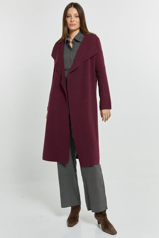 Woman wearing a long burgundy coat over a black and white patterned matching set.