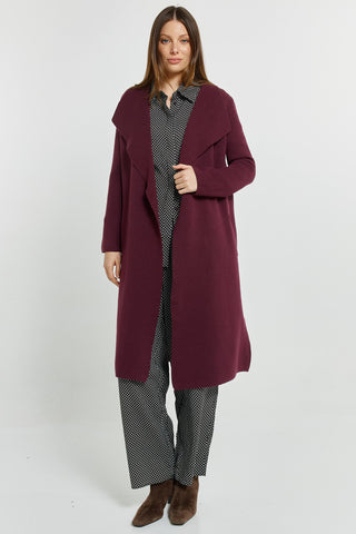 Woman wearing a long burgundy coat over a black and white patterned co-ord set and brown boots