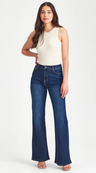 Woman wearing a white ribbed tank top and dark blue flare denim jeans.