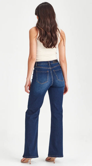 Back view of a woman wearing a white tank top and dark blue flare jeans.