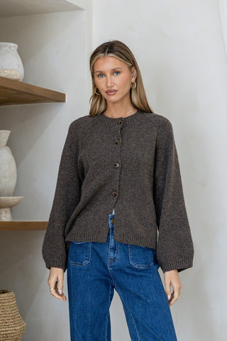 Woman wearing a cozy dark brown button-up knit cardigan and blue denim jeans.
