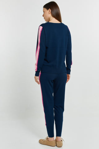 Rear view of a woman wearing a navy blue sweatshirt and joggers with pink side stripes.