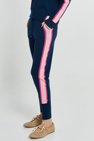 Woman wearing navy blue joggers with pink side stripes and tan ballet flats.