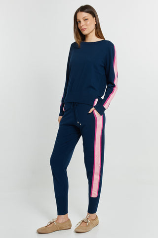Woman wearing navy blue leisure wear set with pink side stripes and beige ballet flats.