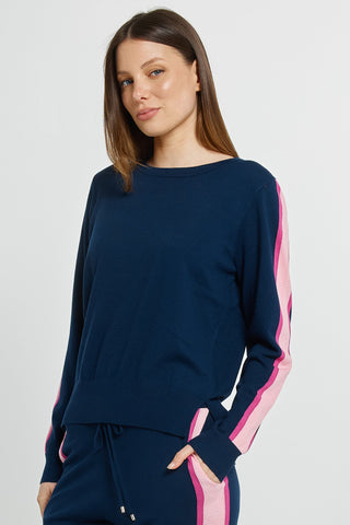 Woman wearing a navy blue long sleeve sweatshirt with pink side stripes and matching joggers.