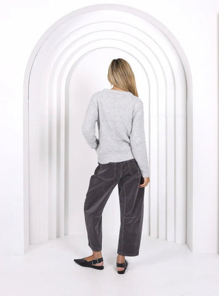 Woman wearing a grey knit sweater and charcoal wide-leg lounge pants standing in an archway.