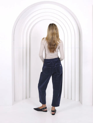 Back view of a woman wearing a beige long-sleeve top and navy blue corduroy pants.