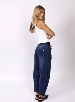 Woman smiling in a white tank top and wide-leg dark denim pants.
