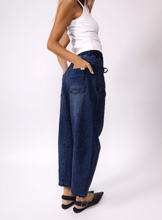 Woman wearing dark wash denim wide leg pants and a white tank top.