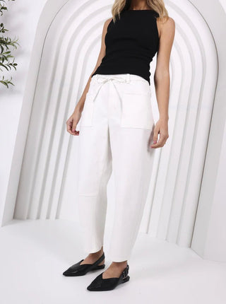 Woman wearing a black sleeveless top and white high-waisted utility pants with black shoes.