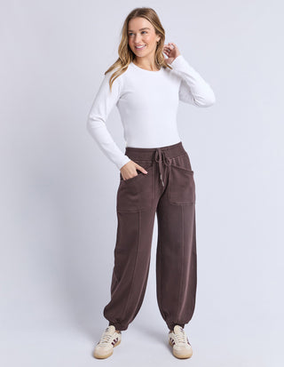 Woman wearing a white long sleeve top and brown wide leg lounge pants with drawstring waist.