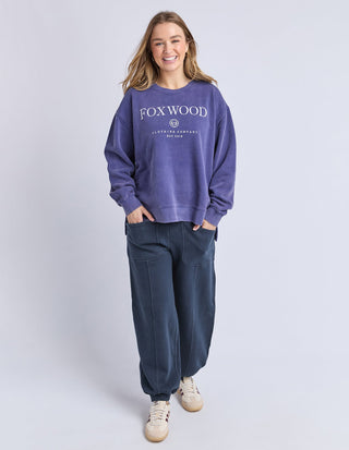 Woman wearing a purple Foxwood sweatshirt and navy blue joggers with beige sneakers.