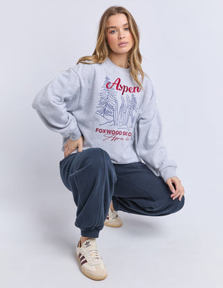 Woman wearing a grey Aspen graphic sweatshirt and navy blue joggers with beige sneakers.
