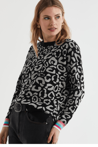 Woman wearing a black and grey leopard print sweater with colorful striped cuffs.