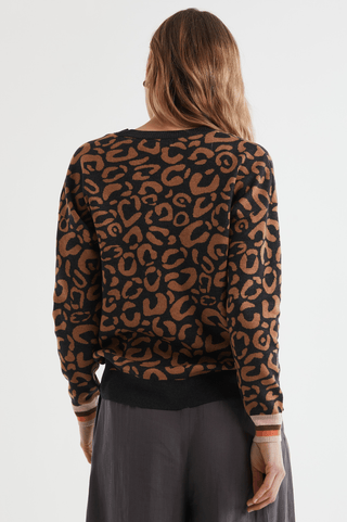 Back view of a woman wearing a brown and black leopard print sweater and charcoal grey pants.