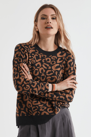 Woman wearing a black and brown leopard print crew neck sweater and grey skirt.