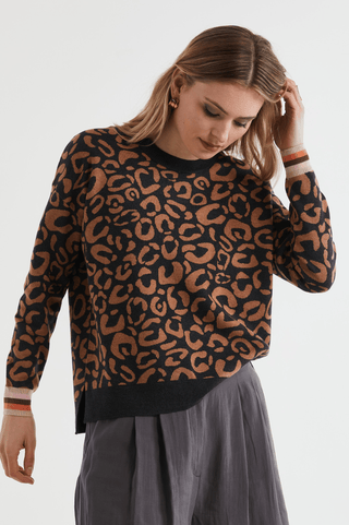 Woman wearing a black and brown leopard print sweater with striped cuffs and grey trousers.