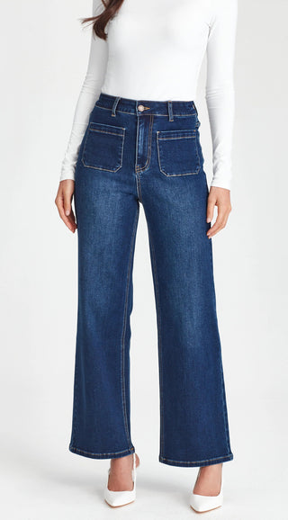 Woman wearing high-waisted dark blue wide leg denim jeans and a white long sleeve top.