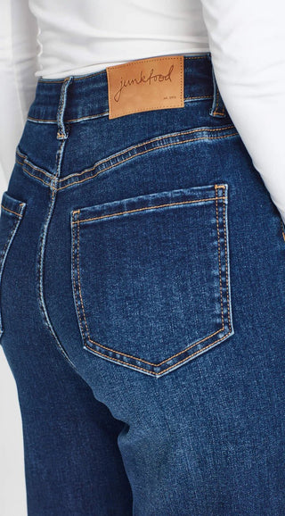 Close-up of blue denim high-waisted jeans with a Junkfood brand leather patch and back pocket.