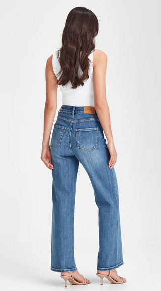 Woman wearing blue high-waisted wide leg denim jeans and a white tank top.