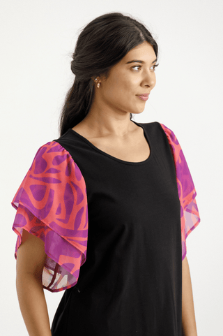Woman wearing a black scoop neck top with vibrant pink and purple patterned flutter sleeves.