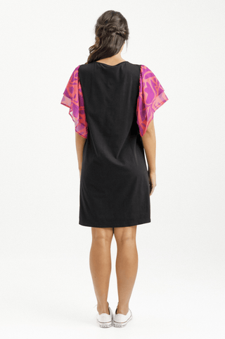 Woman wearing a black mini dress with vibrant pink and purple patterned flutter sleeves.