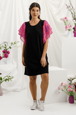 Woman wearing a black short sleeve dress with pink patterned flutter sleeves and white sneakers.