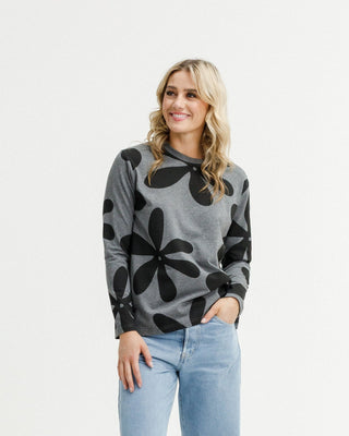 Woman wearing a grey long-sleeve top with black floral print and light blue jeans.