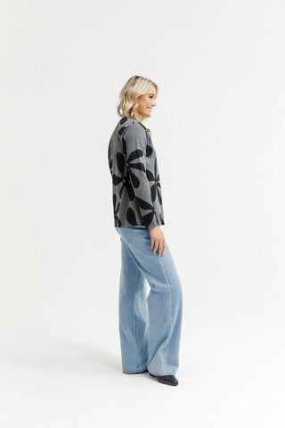 Woman wearing a grey floral print top and light blue wide-leg jeans.