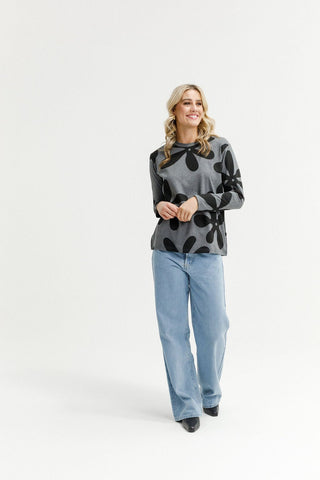 Woman wearing a grey long-sleeve top with black floral patterns and light blue wide-leg jeans.