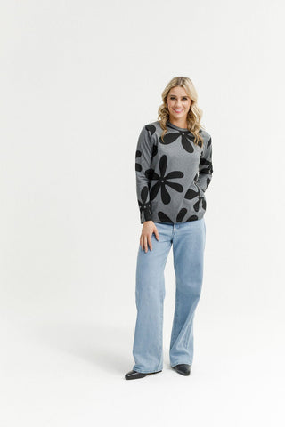 Woman wearing a grey floral print sweatshirt and light wash wide leg jeans.