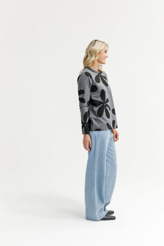 Woman wearing a grey long-sleeved top with large black floral prints and light blue wide-leg jeans