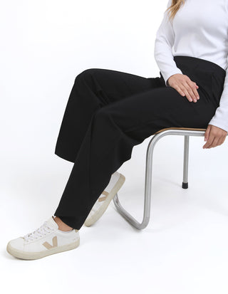 Woman wearing a white long sleeve top, black wide leg trousers, and white Veja sneakers.