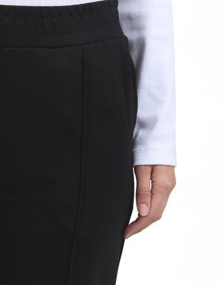 Close-up of a woman wearing a black skirt and a white ribbed long-sleeve top.