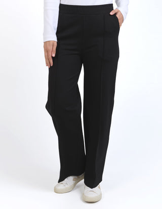Woman wearing black wide-leg trousers with white sneakers and a white top