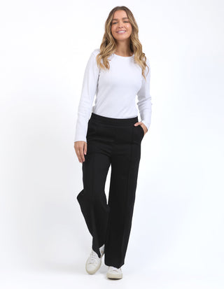 Woman wearing a white long-sleeve top and black wide-leg trousers with white sneakers.