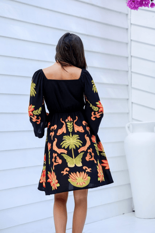 Woman wearing a black long sleeve floral print mini dress with orange and green botanical patterns.