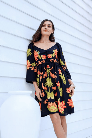 Woman in a black long-sleeve mini dress with vibrant orange and yellow floral embroidery.