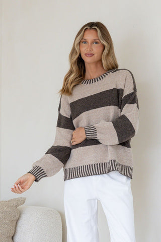 Woman wearing a beige and charcoal striped knit sweatshirt and white pants.